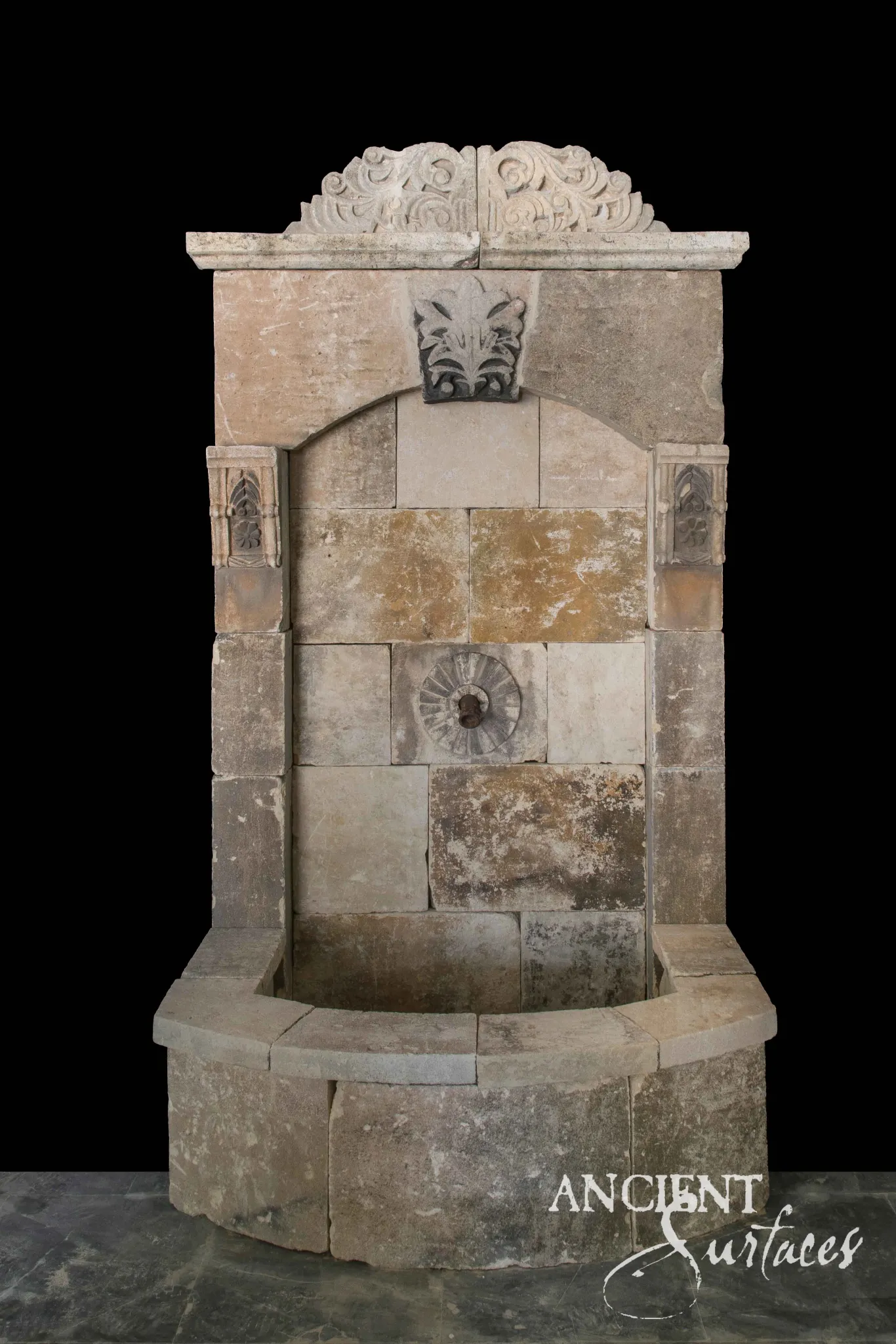 Weathered reclaimed limestone wall fountain with a carved crest and recessed rosette spout